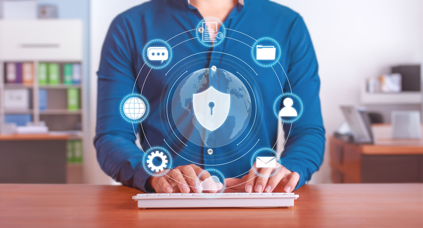 Business professional at a keyboard surrounded by a cybersecurity shield and protection icons